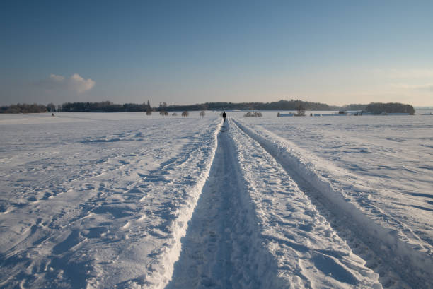 istock Vast landscape in winter. Snow lies on the fields. A path has been cleared through the snow. A village and trees on the horizon. The sky is blue. 1860389808