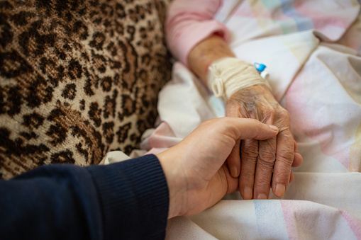 Close-up of a caring family member holding the hand of an ill senior, symbolizing love and connection.