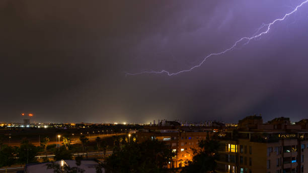 istock Stormy sky raining with a huge lightning bolt drawing a diagonal in the sky on the outskirts of a city over buildings 1860481596
