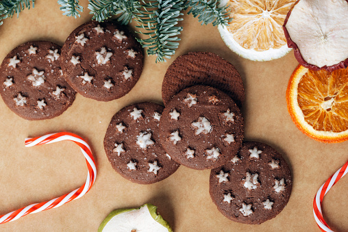Christmas gingerbreads, candy cane, dried fruits and baubles on kraft paper background. Top view, flat lay.