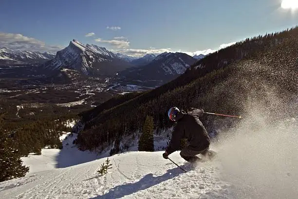 Male Skier enjoys fresh powder in Banff National Park, with the Town of Banff visible in background.