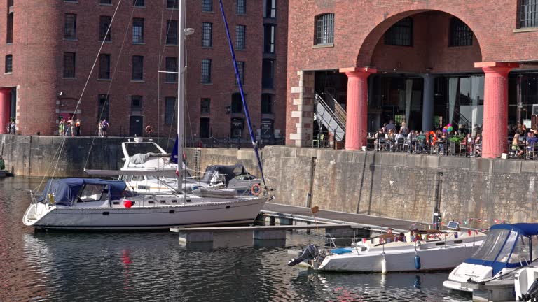 Liverpool, UK - May 20 2023: Boats, yachts docked at Albert Dock next to a covered balcony restaurant full of diners