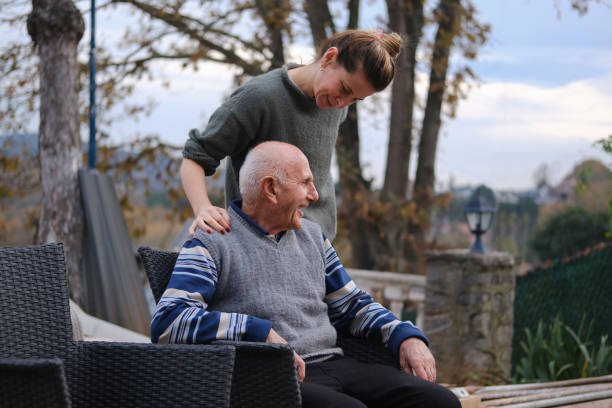 Elderly father and daughter together, sitting in the garden, chatting and having a pleasant time. A young woman chatting with her elderly father in the garden of her house. father daughter 80s stock pictures, royalty-free photos & images