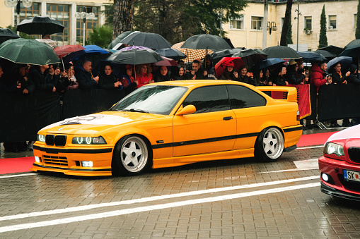 Tirana, Albania - November 28, 2023: On Avenue of Martyrs of the Nation, citizens watch a modified car parade on a rainy Independence Day, featuring a yellow colored BMW 3 E46 and labeled Cair Tuning Team