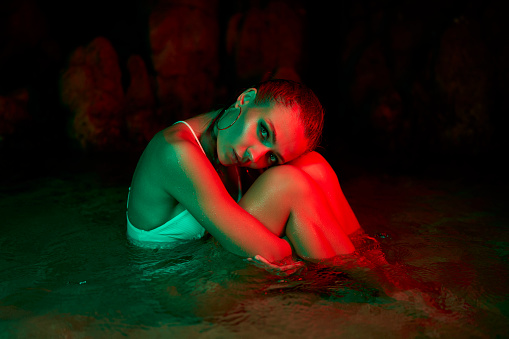 Woman submerged in lagoon at night, vibrant green and red lights. Introspection and emotional depth theme in a tranquil setting. Conceptual art piece emphasizing mental health reflection.