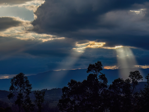 Some sun beams come trough dense clouds, in an overcast sunset over the eastern Andean mountains of central Colombia.