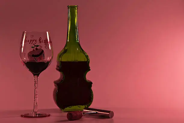 a bottle of wine, wine glass and wine opener on red background.