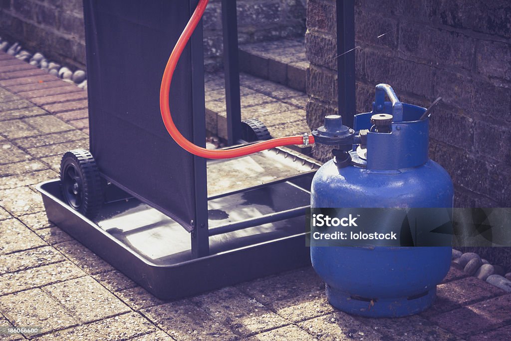 Gas canister and portable barbecue Large blue gas canister attatched to a portable barbecue on wheels in a domestic garden Natural Gas Stock Photo