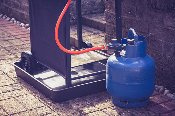 Gas canister and portable barbecue Large blue gas canister attatched to a portable barbecue on wheels in a domestic garden canister photos stock pictures, royalty-free photos & images