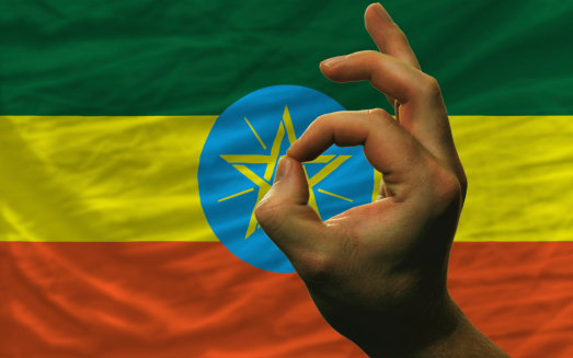 man showing excellence or ok gesture in front of complete wavy ethiopia national flag of  symbolizing best quality, positivity and succes