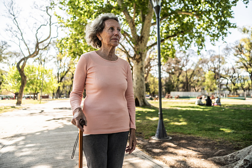 Senior woman using cane walking through the public park