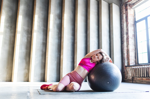 Mid adult woman stretching with fitball in gym