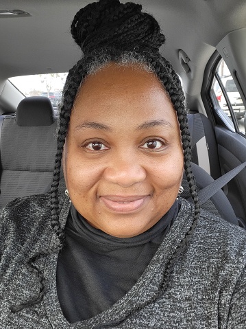 African American Woman in car wearing black and grey with braids selfie.