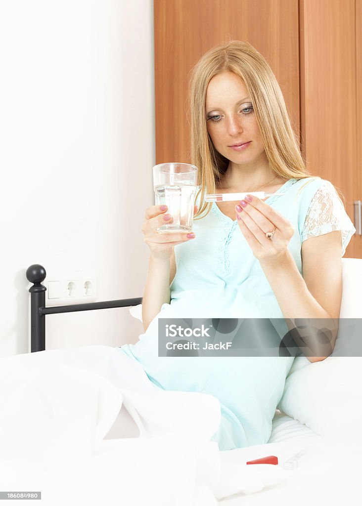 Pregnant woman sitting on bed  with thermometer at home Pregnant woman sitting on bed  with thermometer Adult Stock Photo