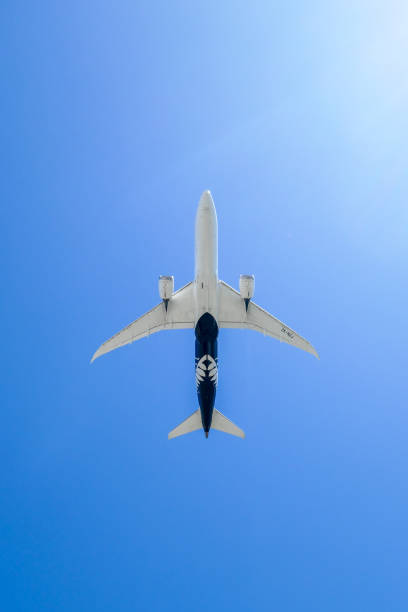 An Air New Zealand Boeing B787-9 plane, registration ZK-NZJ, taking off to the north from the main runway of Sydney Kingsford-Smith Airport and heading to Auckland as flight NZ106. This image was taken from near Nigel Love Bridge, Mascot on a hot, sunny and windy afternoon on 16 December 2023.