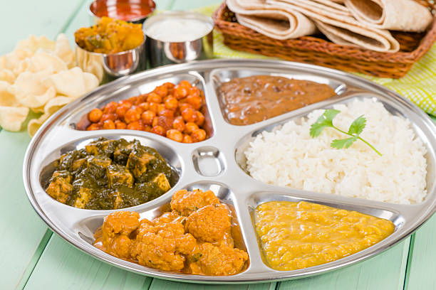 Thali with rice and vegetables on green painted wooden table South Asian selection of vegetarian curries served in a traditional dish with rice, chapatis, poppadoms, yoghurt and chili sauce. nepalese culture stock pictures, royalty-free photos & images