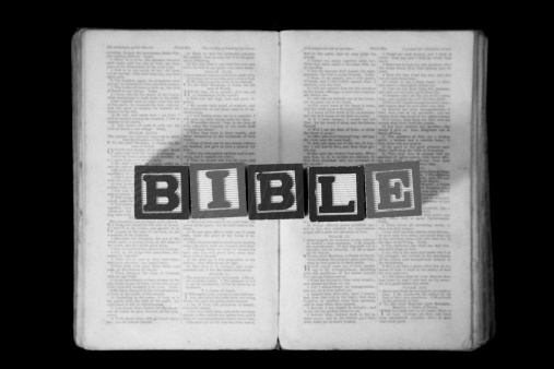 Letter blocks spelling out the word Bible resting on a very old open Bible.  With added film grain effect.