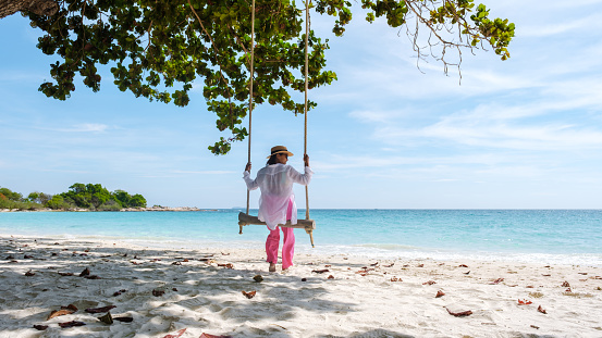 Koh Samet Island Rayong Thailand, the white tropical beach of Samed Island with a turqouse colored ocean, Asian woman on a swing on the beach looking at the ocean