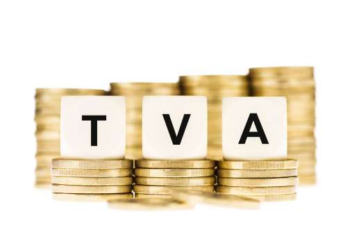 Taxation concept. The letters TVA (French Value Added Tax) on dice on piles of gold coins on a white background.