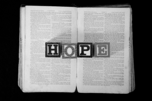 Letter blocks spelling out the word Hope resting on a very old open Bible.  With added film grain effect.