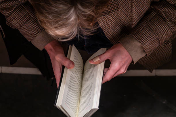 Close up of senior man sits comfortably in an armchair at home, enjoying a good book