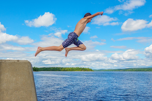 Boy jumping off wharf into water against blue summer sky