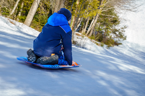 Cute adorable little kid boy enjoy having fun sledging down hill of snow heap snowdrift at alpine mountain skiing resort on bright winter day. Toddler beginner skier rest of training in ski school.