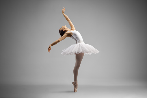 Rear view of young ballerina rehearsing en pointe with trainer watching on the stage