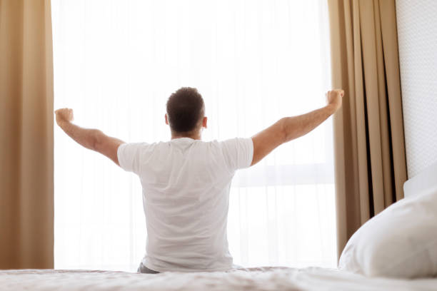 istock Man Waking Up Stretching Hands Sitting In Bedroom, Rear View 1861018409