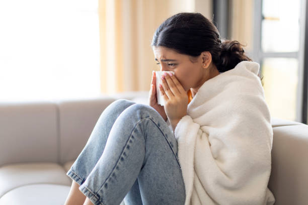 istock Sick Young Indian Woman Blowing Nose In Tissue While Sitting On Couch 1861021396