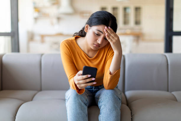 istock Upset Young Indian Woman Looking At Smartphone Screen While Sitting On Couch 1861022278