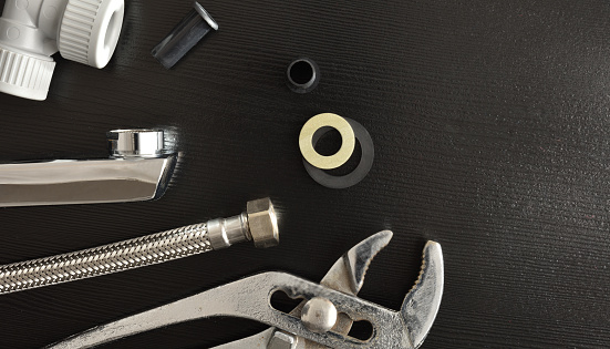 Home plumbing repair concept with tools and accessories on black wooden table. Top view. Horizontal composition.