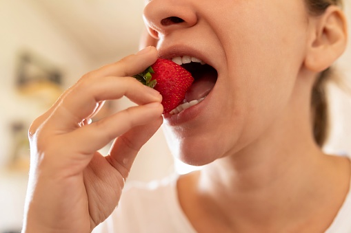 woman puts strawberry in mouth while snacking.