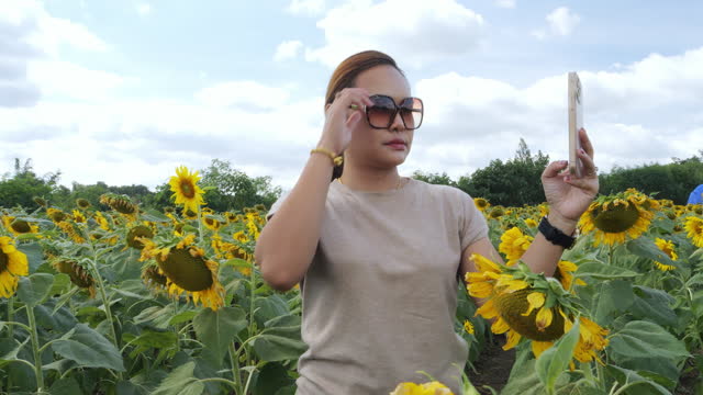 Woman among sunflowers in the field and her use mobile phone to take.