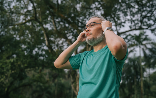 Asian Mature Chinese man put on earphone ready for workout in public park weekend morning