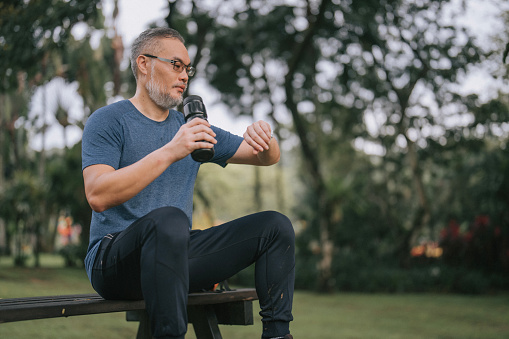 Asian Mature man satisfied with exercise results checking fitness tracker sitting relaxing at public park