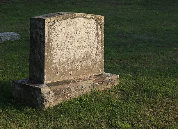 A large gravestone in a graveyard, shot in the golden light of dusk.