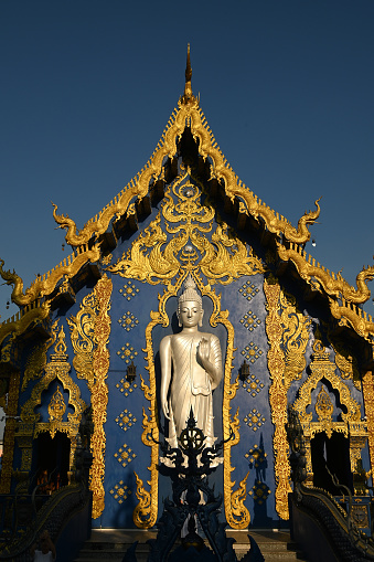 The back of the beauty blue chapel of Wat Rong Suea Ten temple have a large white Buddha image in the forbidding posture. Located Chiang Rai Province in Thailand.