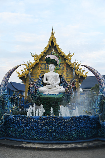 Phra Upakut is a pearl white statue placed in the middle of a fountain under the shade of lotus flowers. In front of the chapel at Wat Rong Suea Ten temple. Located at Chiang Rai province in Thailand.