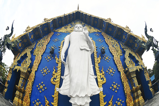 The back of the beauty blue chapel of Wat Rong Suea Ten temple have a large white Buddha image in the forbidding posture. Located Chiang Rai Province in Thailand.