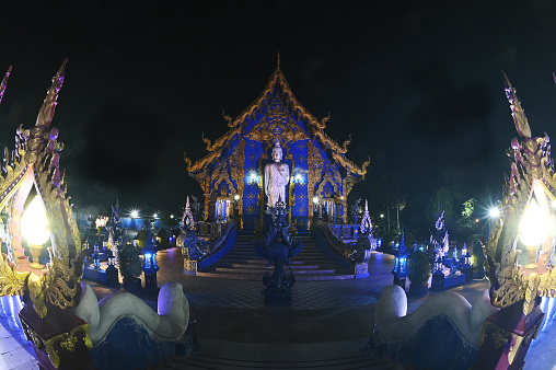 Night scene of large white Buddha image in the forbidding posture at The back of the beauty blue chapel of Wat Rong Suea Ten temple. Located at Chiang Rai Province in Thailand.