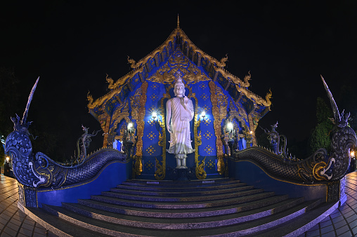 Night scene of large white Buddha image in the forbidding posture at The back of the beauty blue chapel of Wat Rong Suea Ten temple. Located at Chiang Rai Province in Thailand.