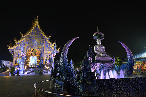 Night scene of Phra Upakut is a pearl white statue placed in the middle of a fountain under the shade of lotus flowers. In front of the chapel at Wat Rong Suea Ten temple. Located at Chiang Rai province in Thailand.