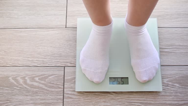 Women's legs in white socks step on the floor scales. 54 kg