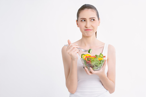Portriat of beautiful young woman holding bowl with salad over isolated whilte background feeling dislike and expression disgusted, woman emotion frustrated with anorexia vegetarian and hate.