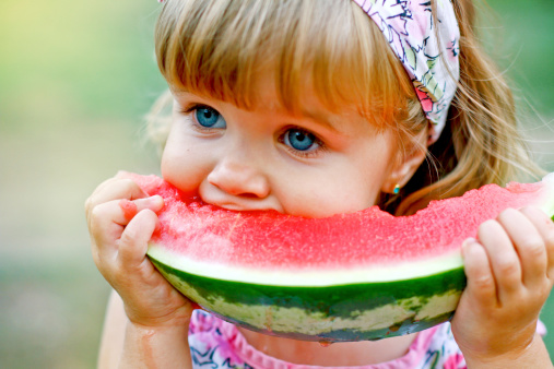 Adorable little girl eats a slice of watermelon outdoors