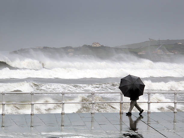 person protecting with umbrella in a rainy and windy day person protecting with umbrella in rainy and windy day walking on promenade with rough sea cyclone rain stock pictures, royalty-free photos & images