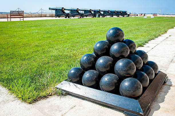 istock Old cannonballs stacked as a pyramid, cannons in background 186117396