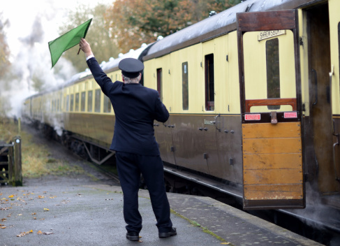 train guard signaling for old steam train to depart from platform, last chance to board