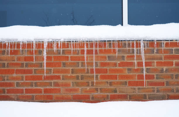 Icicles hang off eavestrough in sunlight and lofty clouds in sky